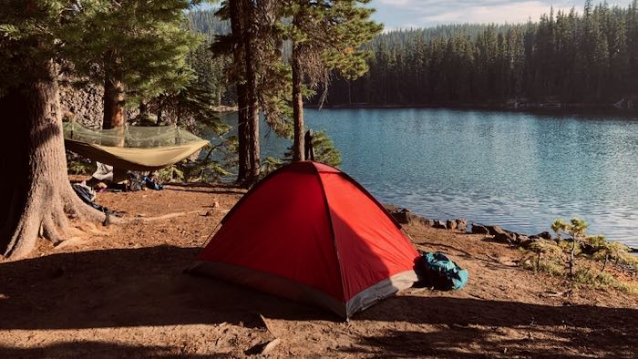 red 4 person tent is standing next to the lake
